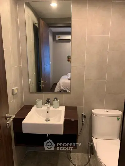 Modern bathroom with sleek sink and mirror, neutral tiles, and contemporary fixtures.