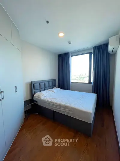 Modern bedroom with large window and wooden flooring in a stylish apartment.