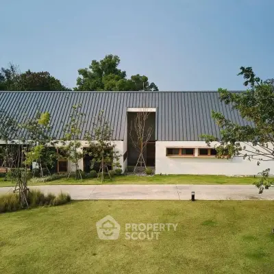Modern minimalist house with sleek metal roof and lush green lawn, surrounded by trees.