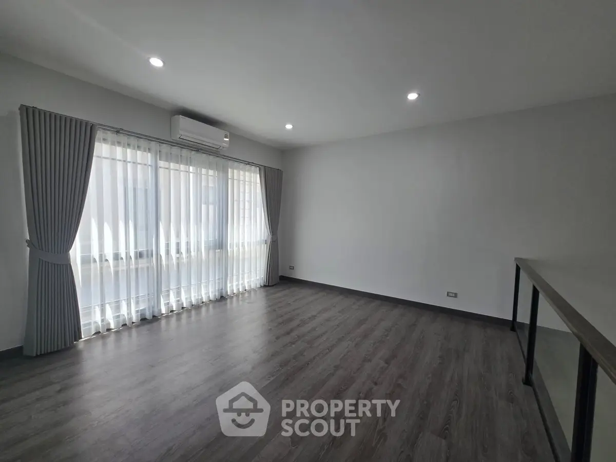 Spacious empty room with large window and modern flooring, perfect for customization.