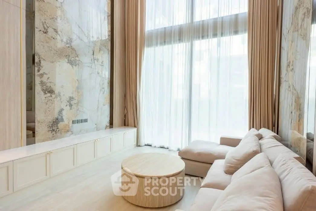 Luxurious living room with high ceilings and elegant marble walls, featuring a cozy sectional sofa and natural light.