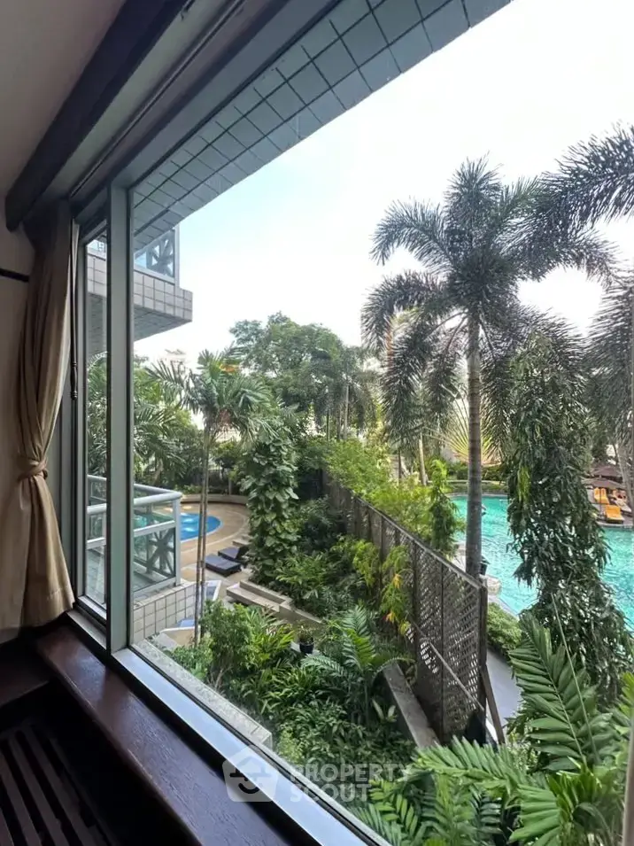 Stunning poolside view from a window overlooking lush greenery and palm trees.