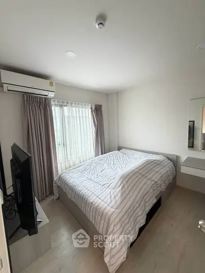 Cozy bedroom with natural light, featuring a comfortable bed and modern air conditioning unit.