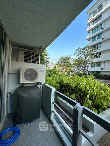 Modern balcony with air conditioning unit and lush greenery view in urban setting.