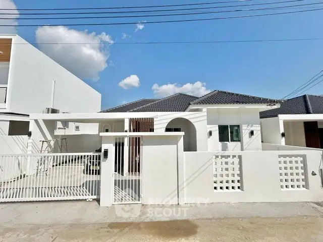 Modern white exterior of a single-story house with gated entrance and tiled roof under a clear blue sky.