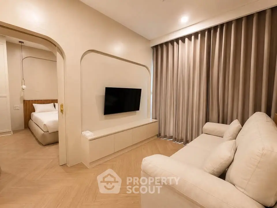 Modern living room with cozy sofa and wall-mounted TV, adjacent to a stylish bedroom.