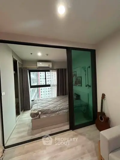 Modern bedroom with glass partition and city view, featuring cozy decor and natural light.
