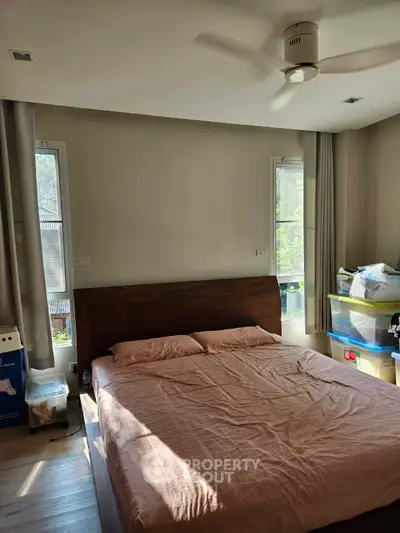 Cozy bedroom with natural light and ceiling fan, featuring a comfortable bed and organized storage.