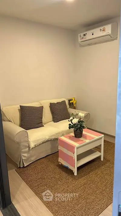 Cozy living room with sofa, air conditioning, and small coffee table, perfect for relaxation.