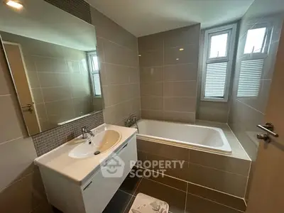 Modern bathroom with sleek tiles and bathtub, featuring natural light from large windows.