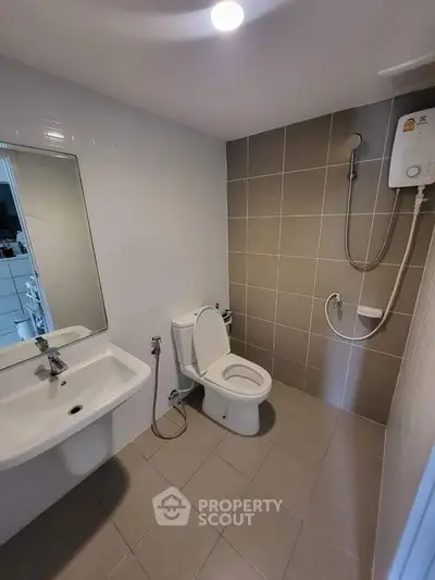 Modern bathroom with shower, toilet, and sink in a tiled setting.