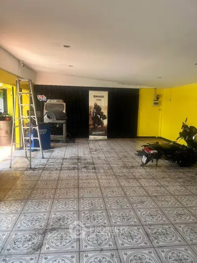 Spacious garage with decorative tiled flooring and vibrant yellow walls, featuring a motorcycle and ladder.
