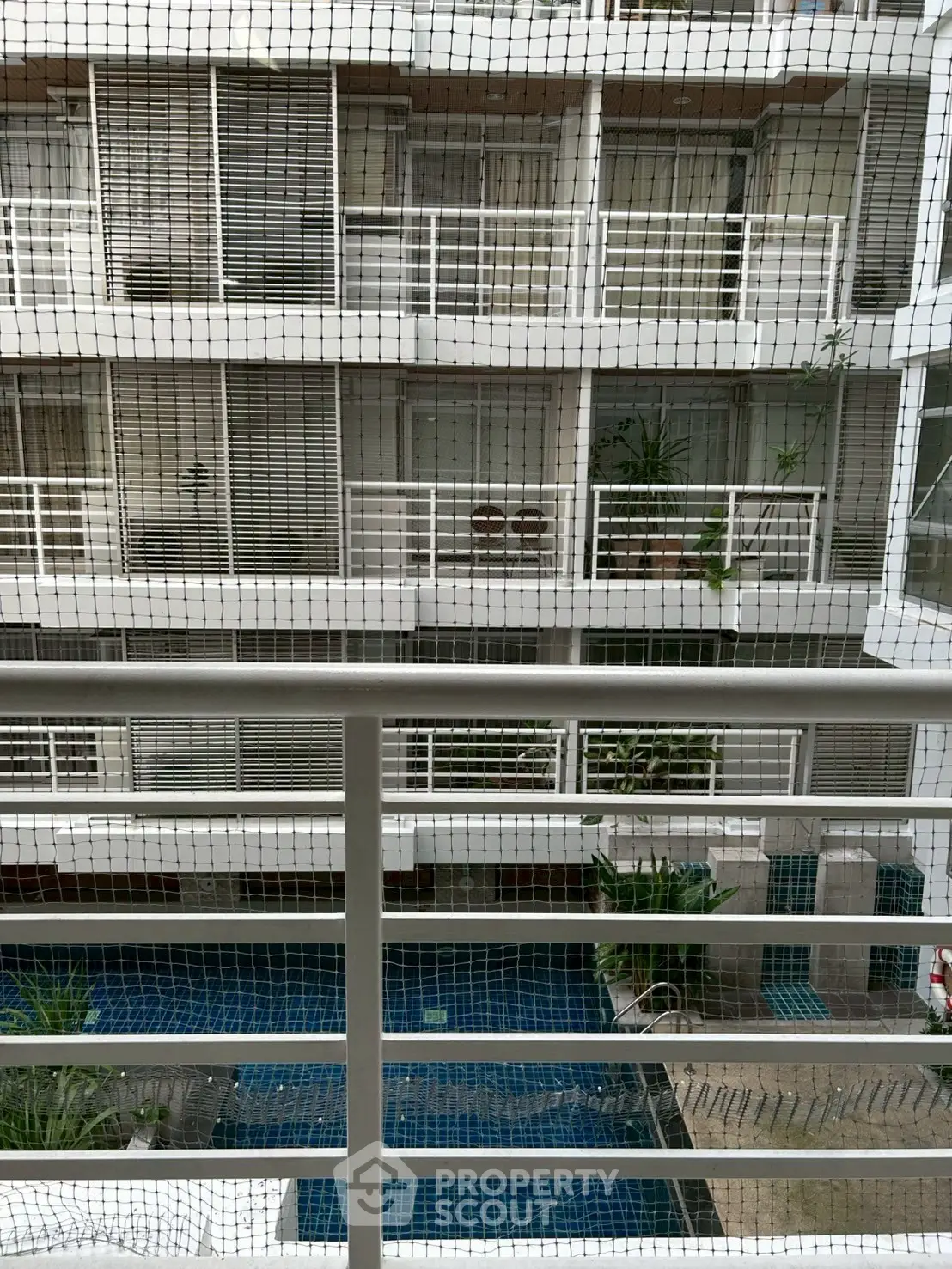 Modern apartment building with pool view from balcony, featuring sleek railings and greenery.