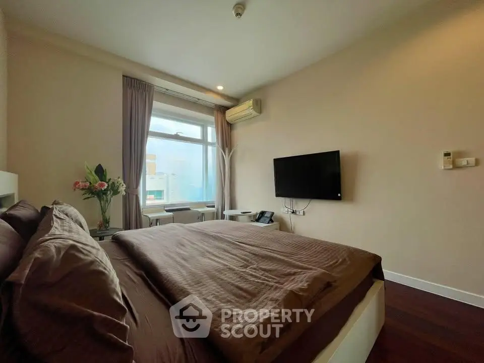Modern bedroom with large window and wall-mounted TV in stylish apartment.