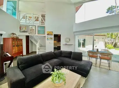 Spacious living room with high ceilings and large windows overlooking a lush garden, featuring modern decor and cozy seating.