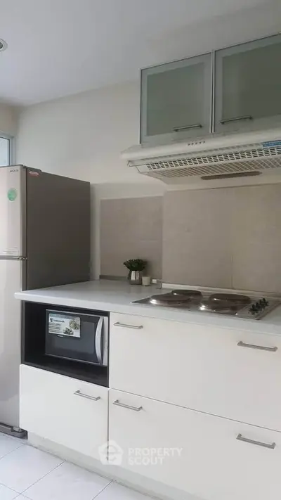 Modern kitchen with sleek white cabinets, built-in microwave, and stainless steel fridge.