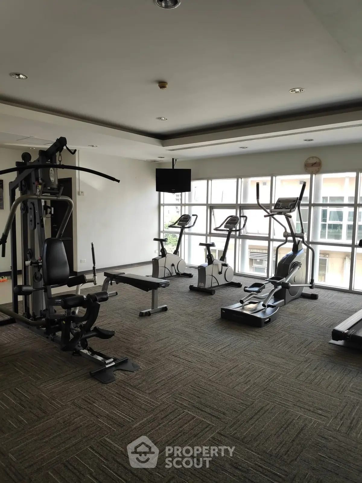 Spacious gym with modern exercise equipment and large windows for natural light.