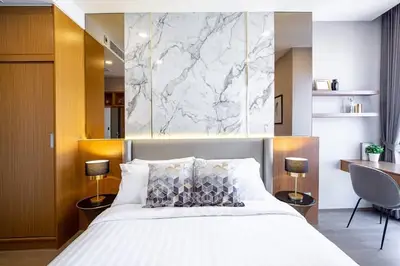 Modern bedroom with stylish decor, marble accent wall, and cozy lighting in a luxury apartment.
