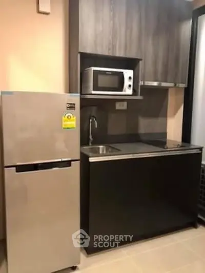 Modern compact kitchen with fridge, microwave, and sleek cabinetry.