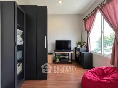 Modern living room with sleek black furniture and large window, featuring a cozy bean bag and TV setup.
