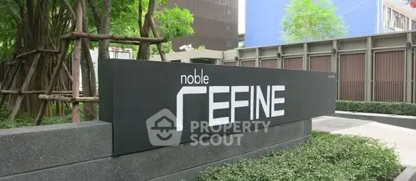 Modern building entrance with sleek signage and lush greenery.