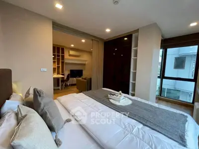 Modern bedroom with cozy decor and open layout leading to living area, featuring large windows for natural light.
