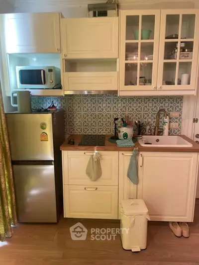 Charming kitchen with white cabinets, microwave, and fridge in cozy apartment.