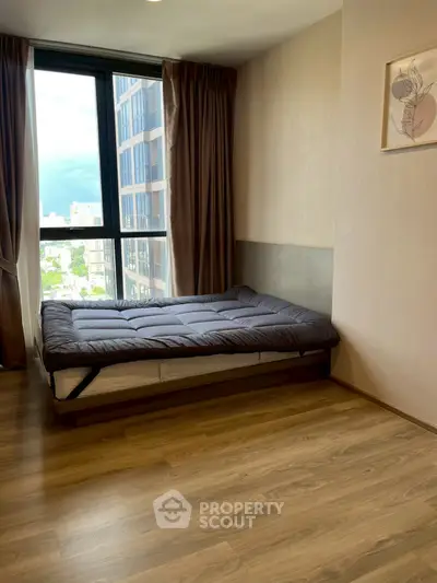 Modern bedroom with large window and wooden flooring in a high-rise apartment.