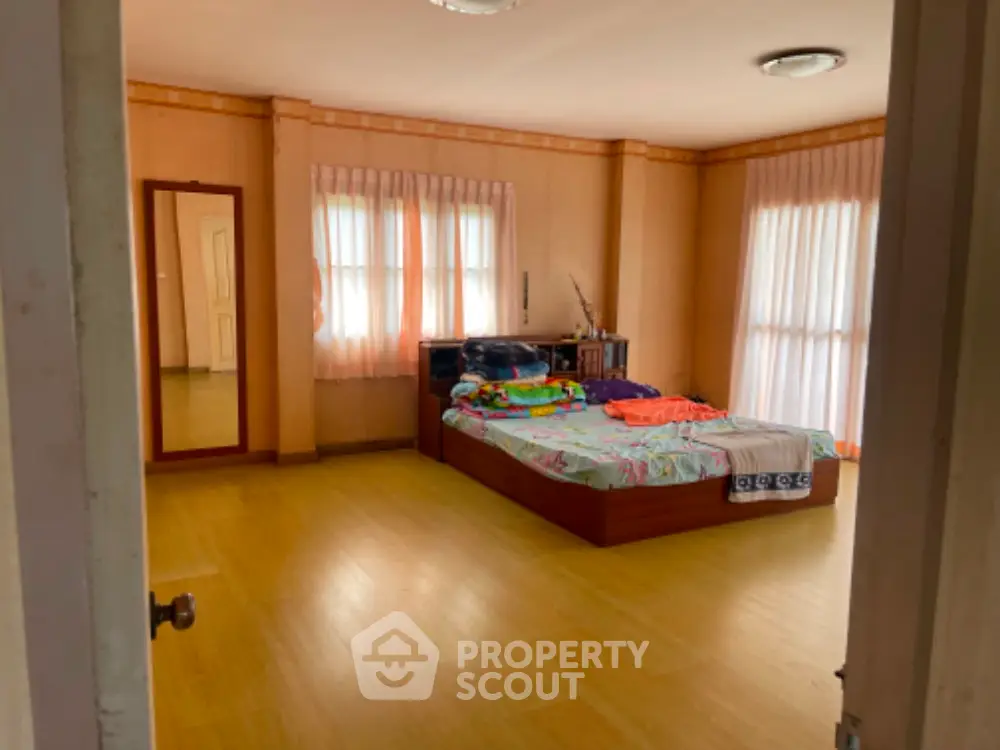 Spacious bedroom with polished wooden floors, ample natural light, and warm-toned walls, offering a serene and comfortable living space.