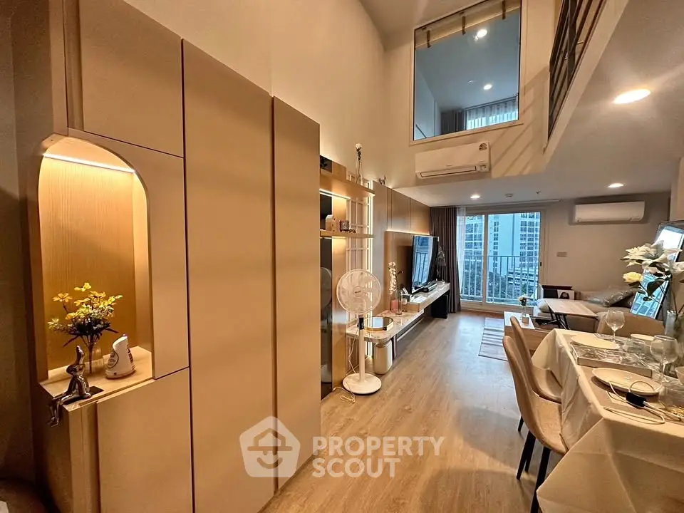 Modern living room with open layout and stylish decor, featuring a dining area and large windows for natural light.