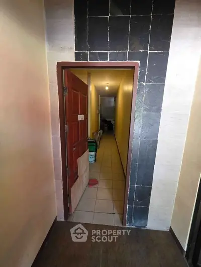 Narrow hallway entrance with tiled walls and wooden door, leading to interior space.