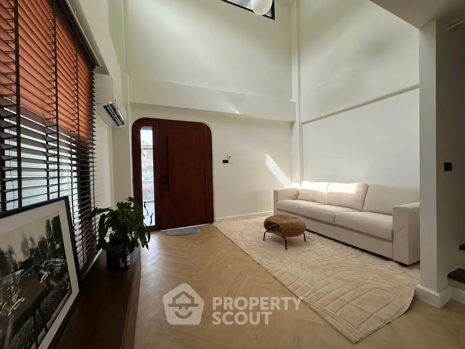 Spacious living room with high ceiling, modern decor, and natural light