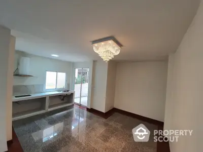 Spacious living room with polished terrazzo flooring, elegant chandelier, and ample natural light streaming through large windows, leading to a cozy balcony.