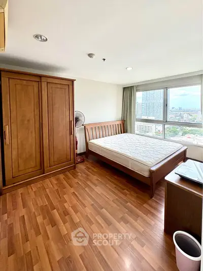 Spacious bedroom with wooden flooring and city view, featuring a large wardrobe and comfortable bed.