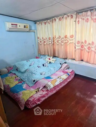 Cozy bedroom with wooden flooring and air conditioning, featuring colorful bedding and floral curtains.