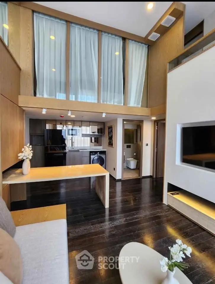Modern duplex living room with high ceilings and open kitchen layout, featuring sleek wooden finishes and stylish decor.