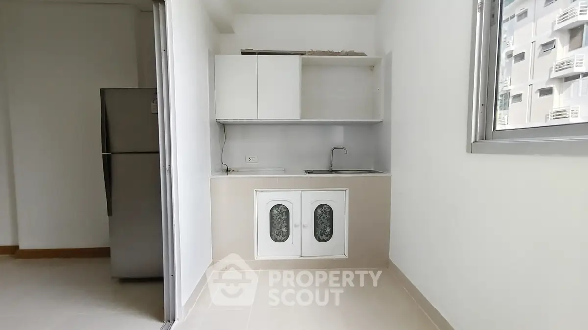 Modern minimalist kitchen with sleek cabinetry and stainless steel fridge in a bright apartment.