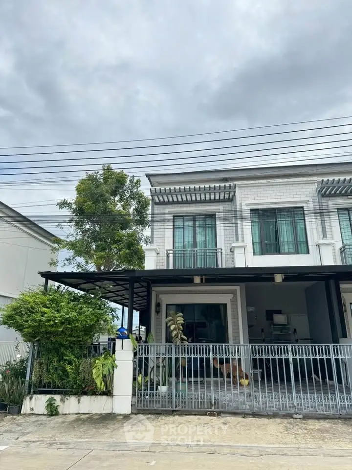 Modern two-story townhouse with gated front yard and lush greenery under a cloudy sky.