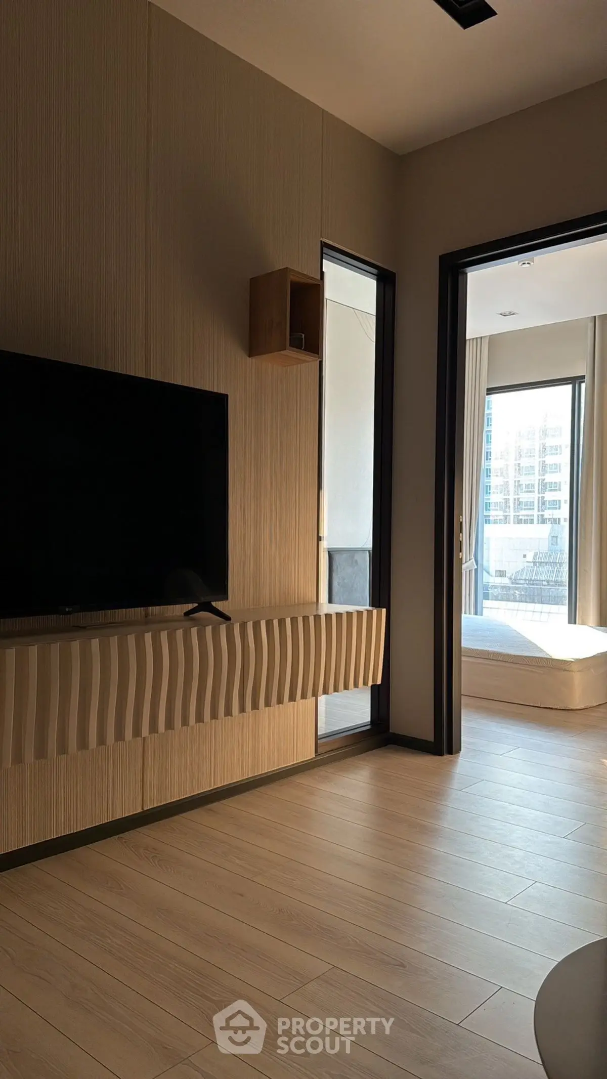 Modern living room with sleek TV setup and view of sunlit balcony.