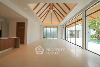 Spacious modern living room with high ceilings and large windows overlooking a pool.