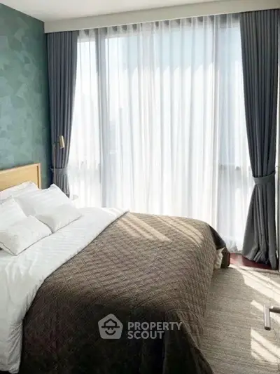 Bright and airy bedroom with large windows and elegant curtains, featuring a cozy bed and stylish decor.