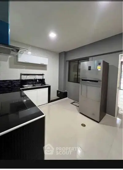 Modern kitchen with sleek appliances and minimalist design, featuring a stainless steel fridge and ample counter space.