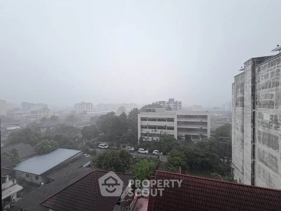 Panoramic cityscape view from a high vantage point on a rainy day, showcasing urban buildings and lush greenery.