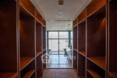 Spacious walk-in closet with wooden shelves leading to a bright bathroom with a large window.