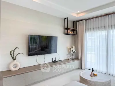 Modern living room with wall-mounted TV and elegant decor, featuring large windows with sheer curtains.