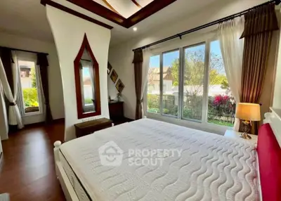Spacious bedroom with large window and elegant decor, offering a serene garden view.