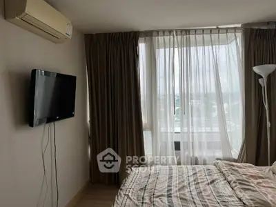 Cozy bedroom with large window and wall-mounted TV, featuring neutral tones and natural light.