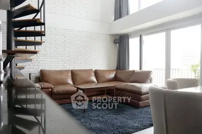 Spacious modern living room with leather sofa and spiral staircase, featuring large windows for natural light.