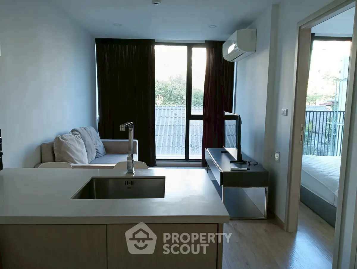 Modern apartment interior with open kitchen and cozy living area, featuring large windows and natural light.