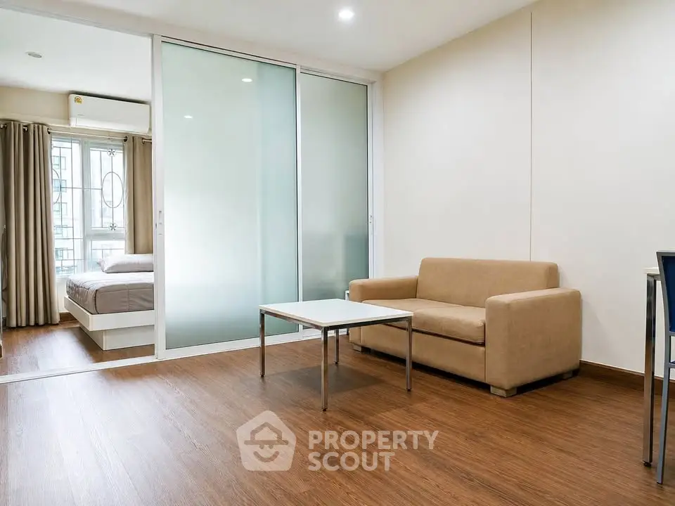 Modern apartment with open living room and bedroom, featuring wooden flooring and minimalist furniture.